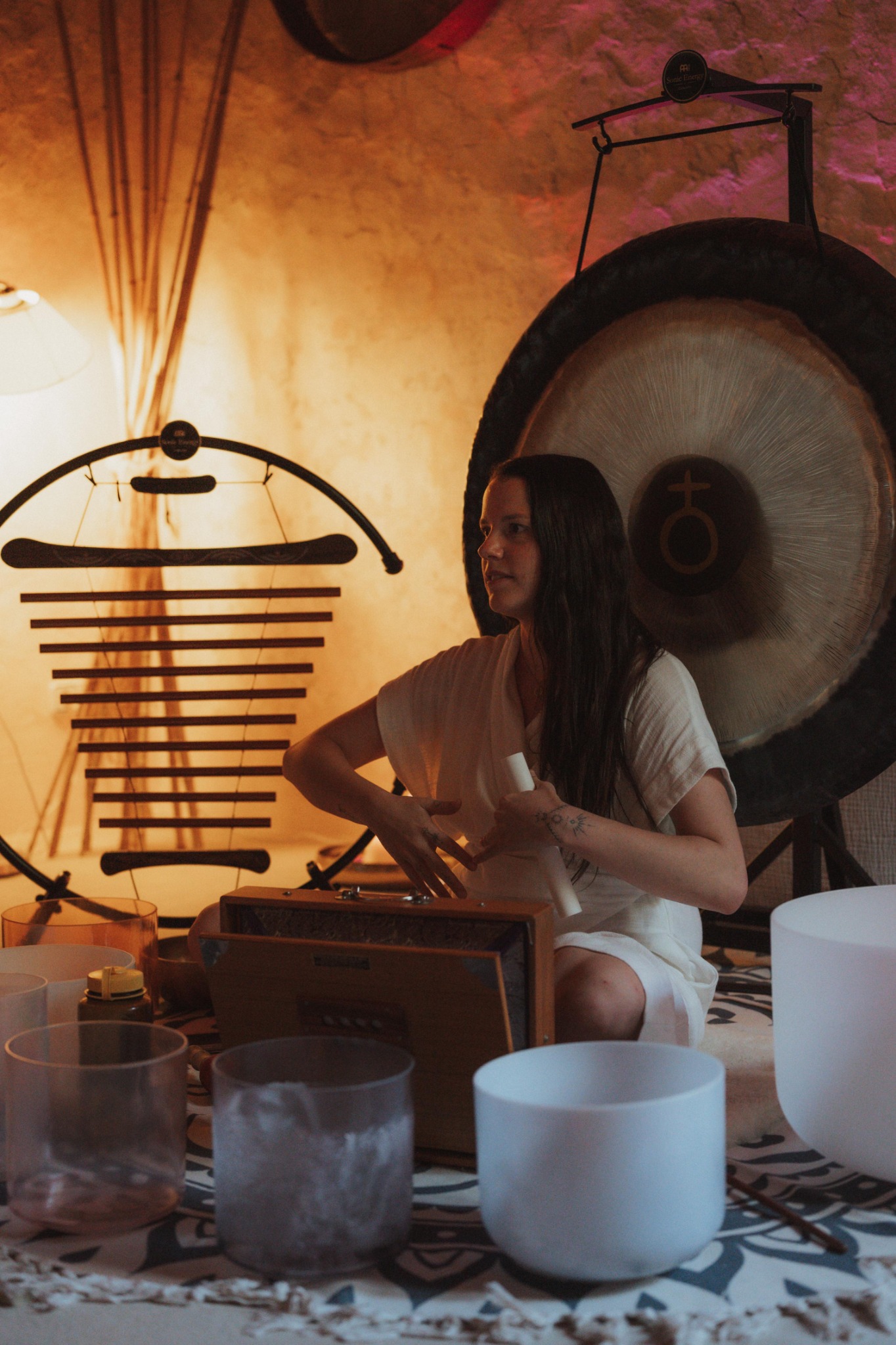 Anna seated with singing bowls, chimes and a gong in a warmly lit room