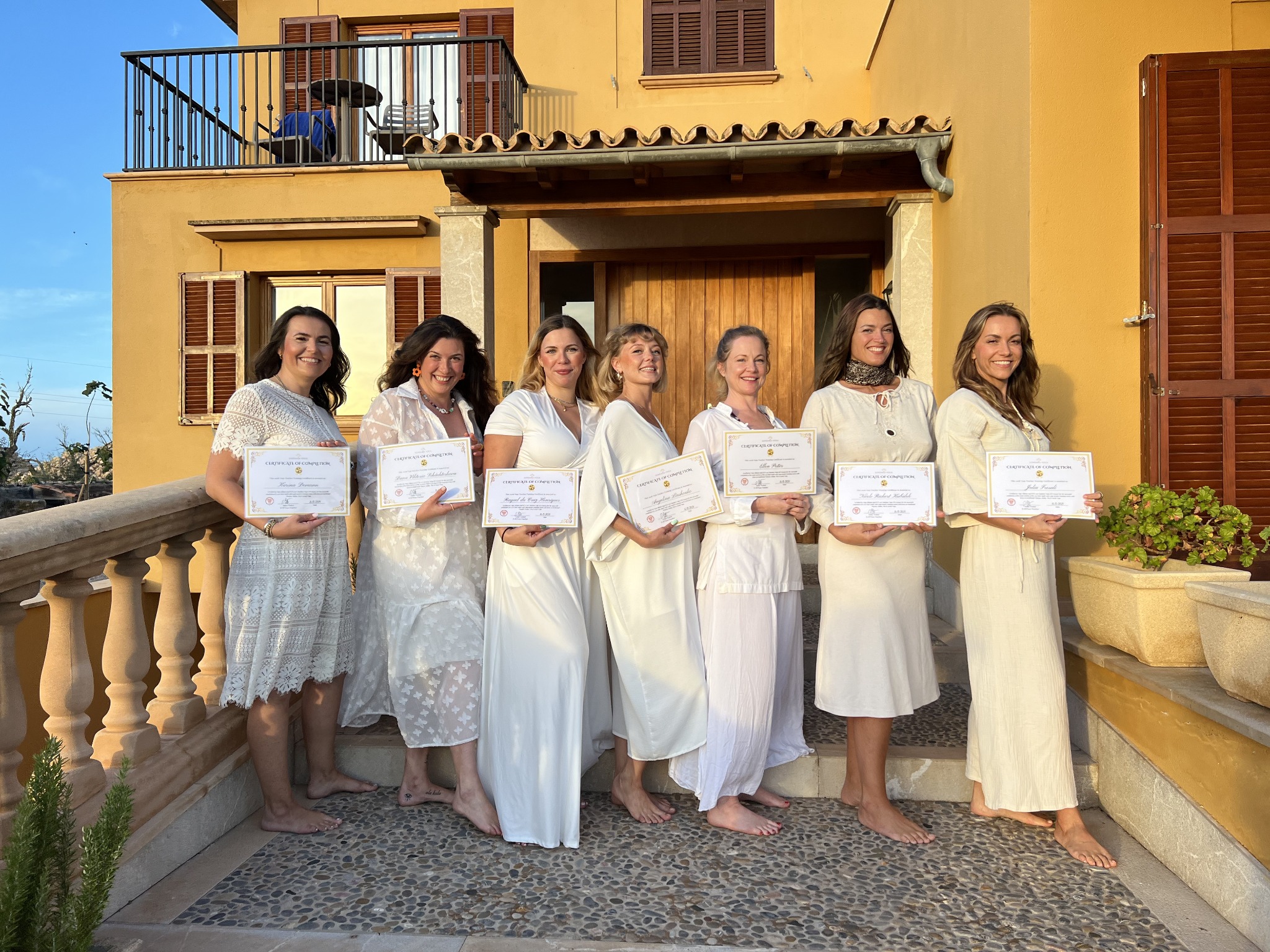 Yoga training graduates holding their certificates outside a sunlit Mallorcan villa